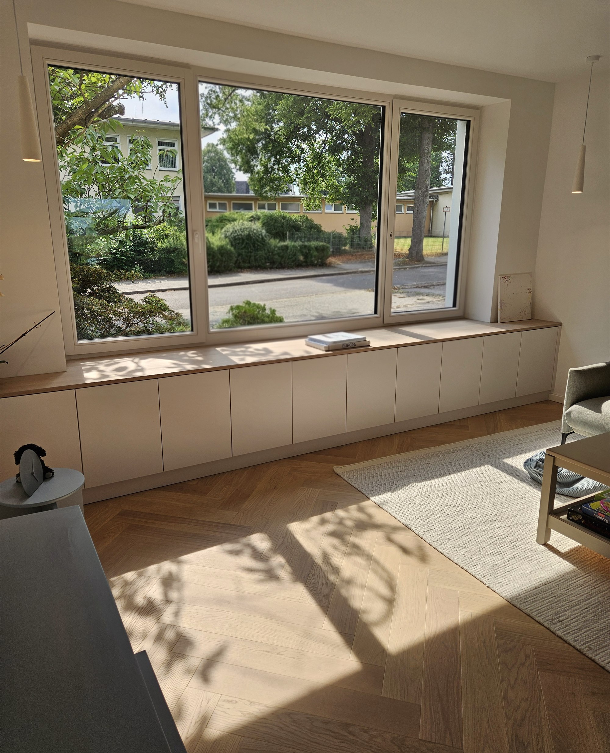 Maßgefertigte Lowboard-Anlage unter der Fensterfront mit Sonnenlicht auf Parkett, Essen