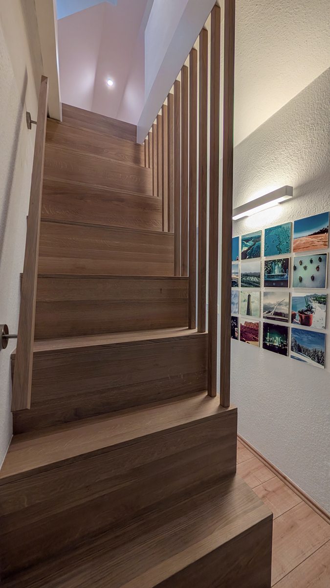 Blick von unten auf die Eichentreppe in Faltwerk-Optik mit Holzlamellen und Handlauf an der Wand